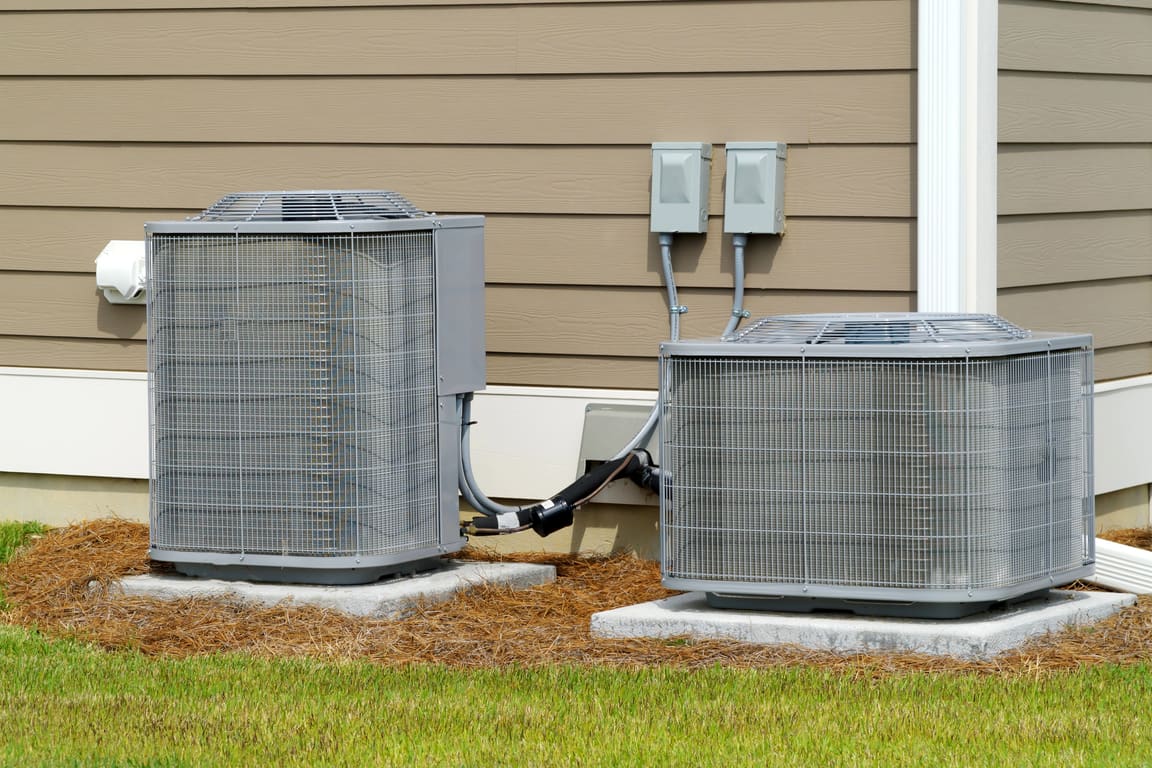 Two central air condensers on pads beside lap siding