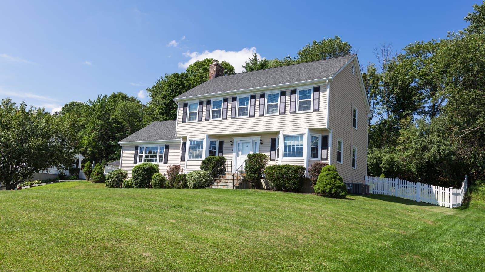 Gray colonial house with a central air conditioner beside a white fence