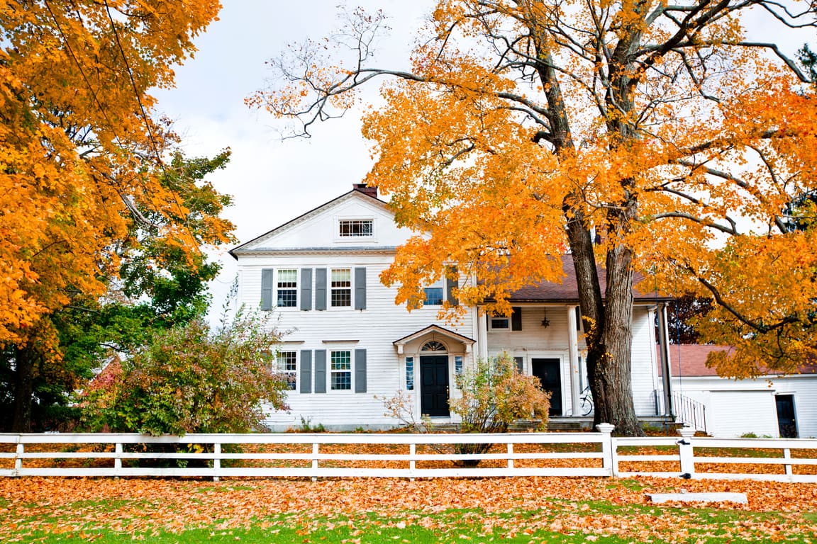 White colonial house behind a rail fence under orange fall maples