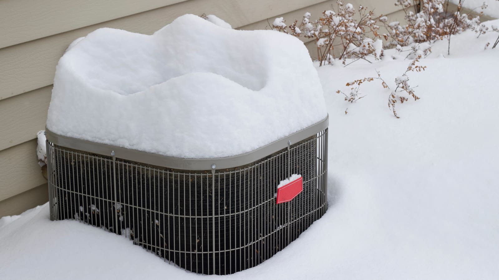 Outdoor condenser capped with deep snow beside a house