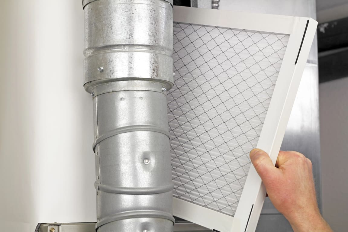 Hand sliding a pleated filter out of a furnace