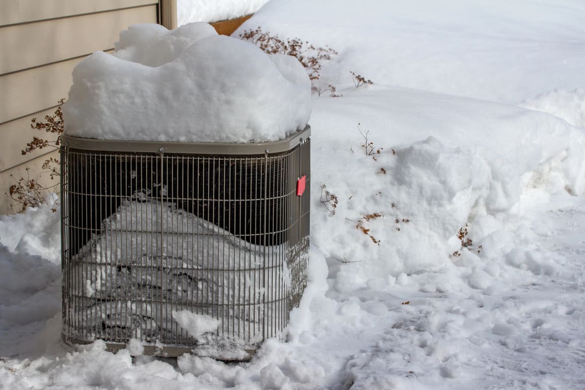 Outdoor unit buried in snow beside a house