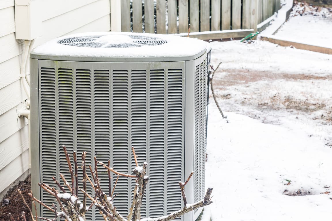 Condenser dusted with snow beside house siding