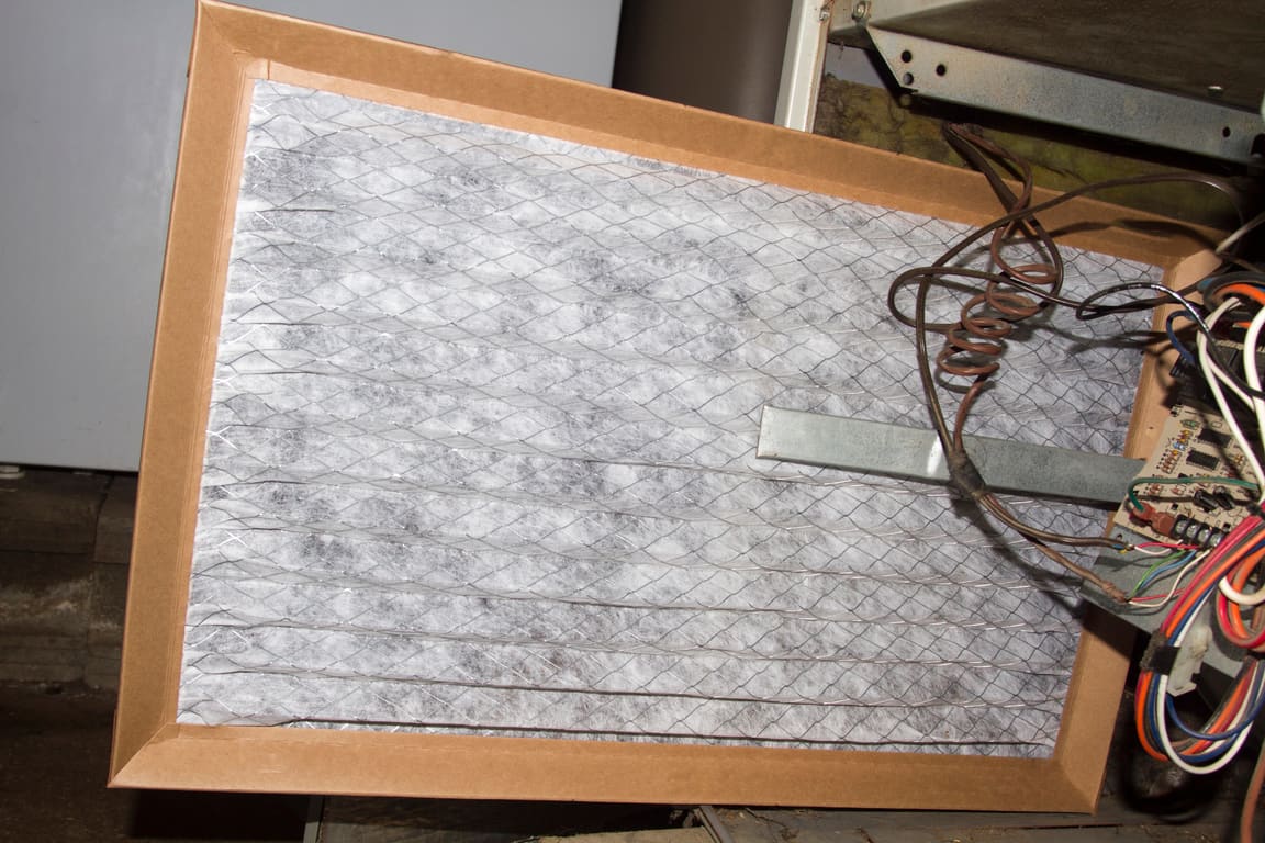 Dirty pleated furnace filter pulled out in front of the furnace wiring